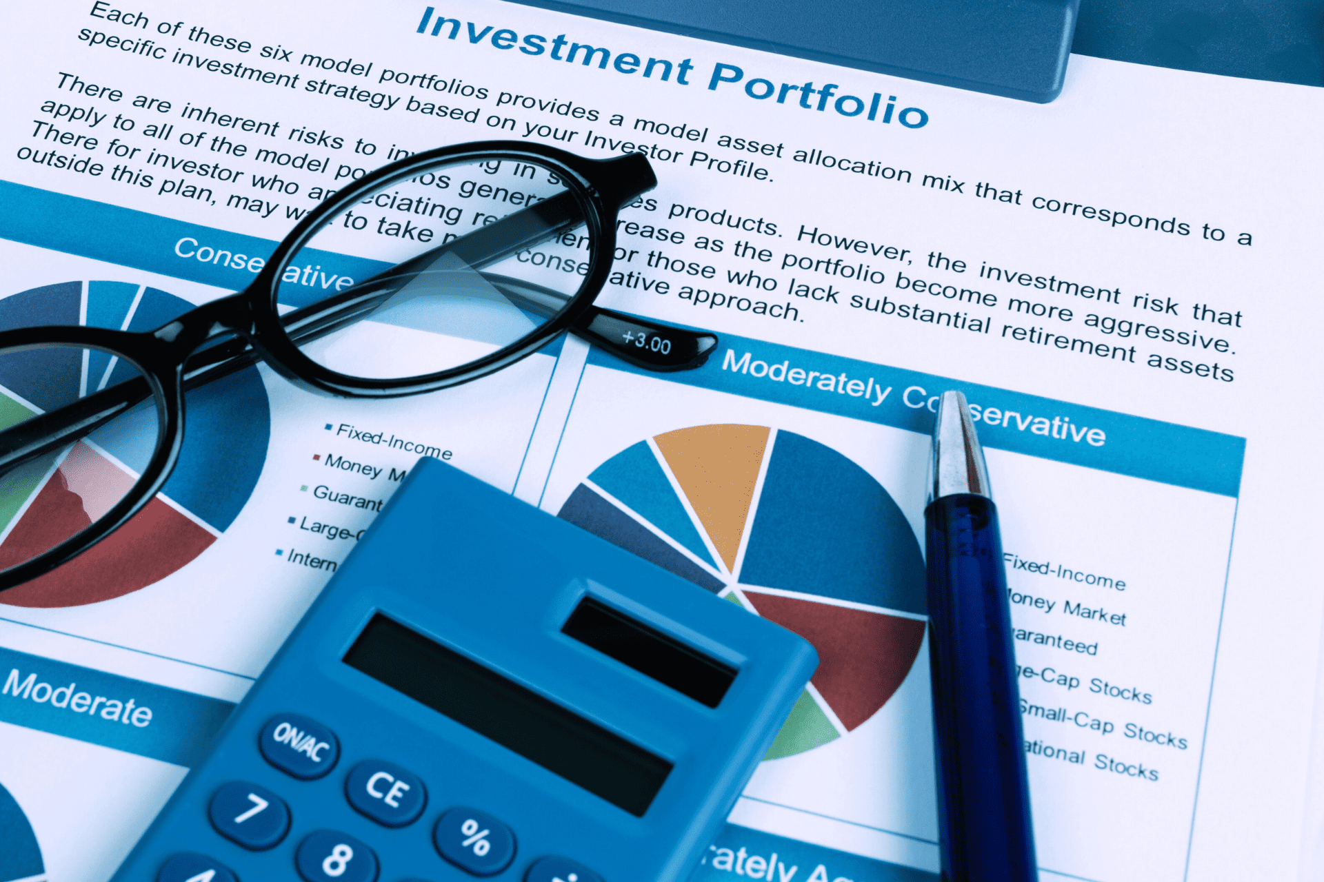 Investment portfolio analysis with pie charts, calculator, pen, and eyeglasses on financial documents.